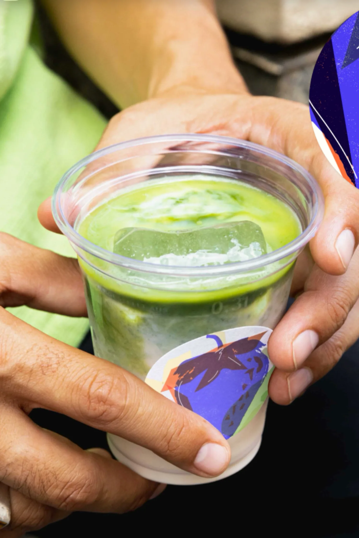 Hands sharing an iced matcha drink in a daytime social occasion